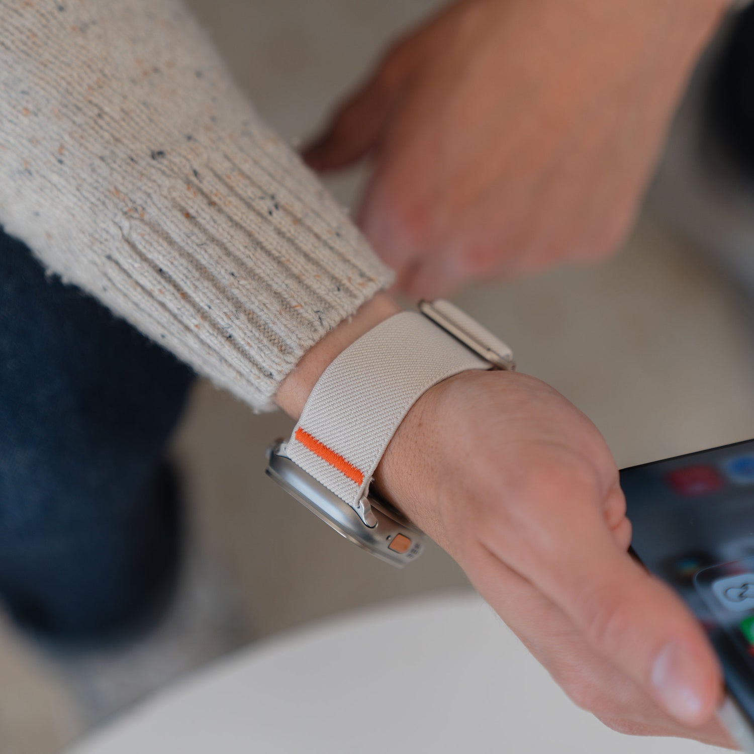 Eine Person passt ihr Arktisband Apple Watch Nylonarmband "FlexOne" an, während sie in der anderen Hand ein Smartphone hält.