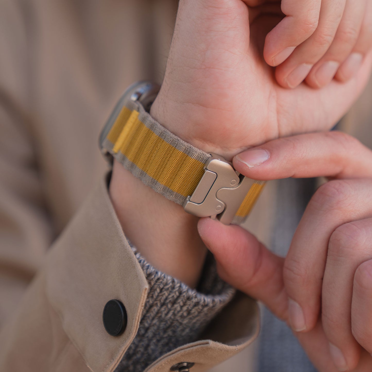 Eine Person befestigt ein gelb-grau gestreiftes Arktisband Apple Watch Armband "CoreX" mit einem Parachute-Verschluss an ihrem Handgelenk.