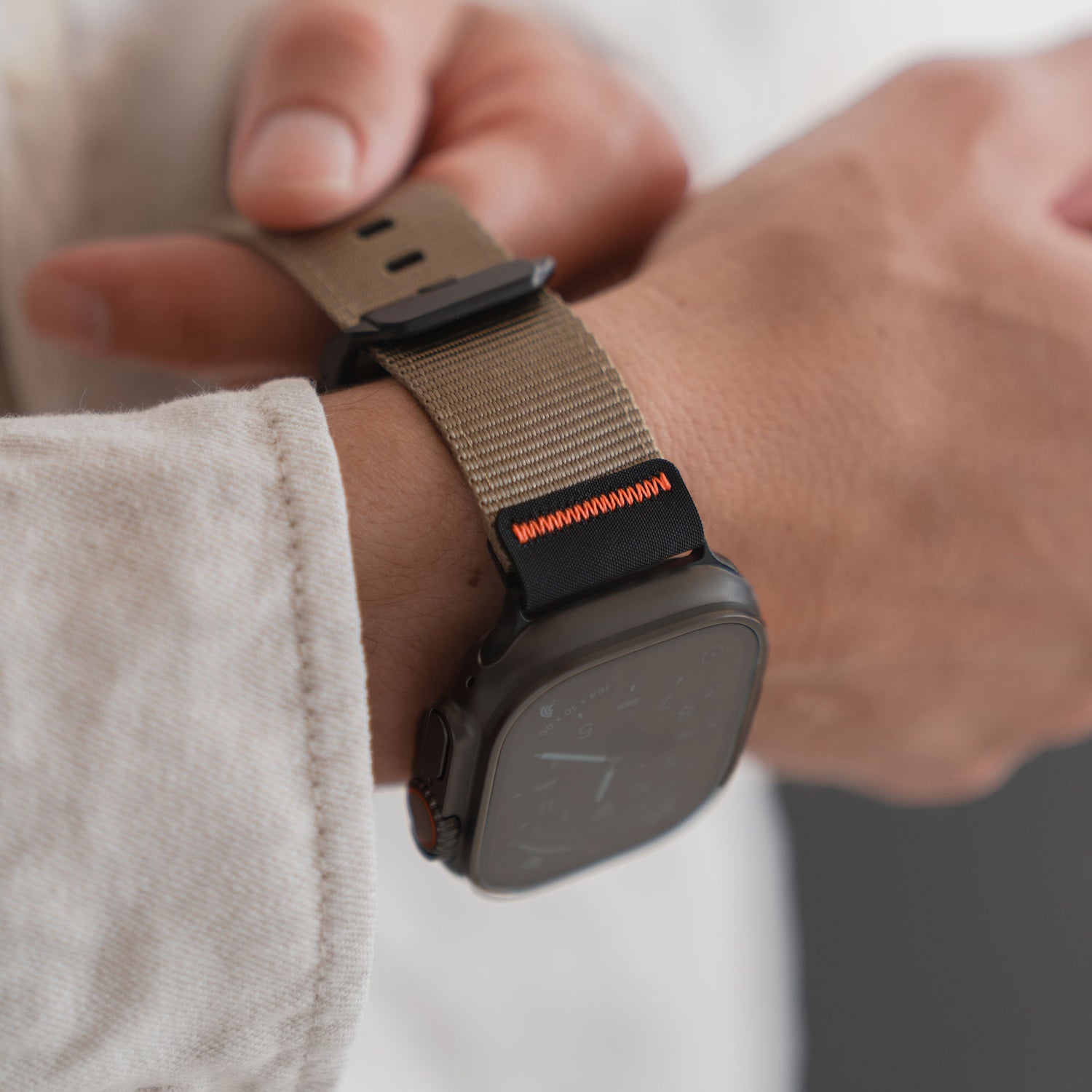 Jemand passt sein arktisband Apple Watch Armband "Terra" mit beigem Outdoor-Nylongewebe, extrabreitem 24-mm-Gewebe und orangefarbenen Nähten an sein Handgelenk an.
