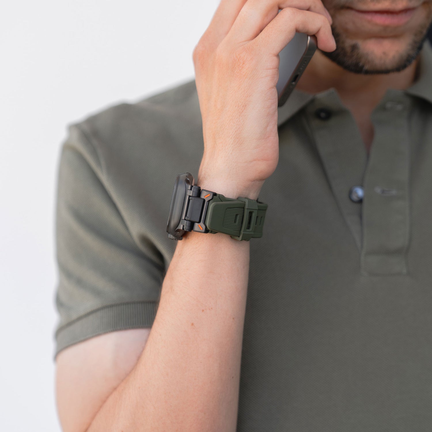 Eine Person im olivgrünen Poloshirt hält ein Smartphone ans Ohr und trägt das Arktisband Apple Watch Ultra Armband „Atlas“ mit markanten Edelstahlelementen. Nur der untere Teil ihres Gesichts ist sichtbar.