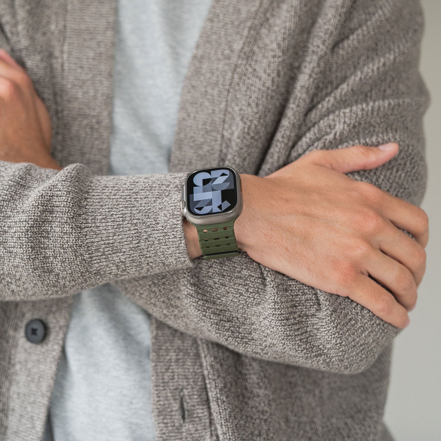 Eine Person in einer strukturierten beigen Strickjacke und einem grauen Hemd zeigt ihren linken Arm und trägt ein magnetisches Silikonarmband „Power“ von arktis für die Apple Watch mit einer großen digitalen Zeitanzeige auf dem Bildschirm der Apple Watch.