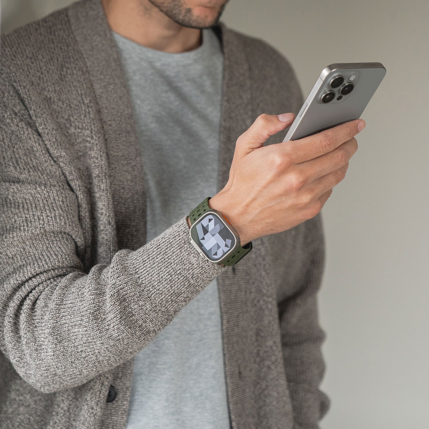 Eine Person in einer grauen Strickjacke und einem T-Shirt hält ein Smartphone und trägt ein grünes magnetisches Silikonarmband „Power“ für die Apple Watch mit einer großen digitalen Uhranzeige.