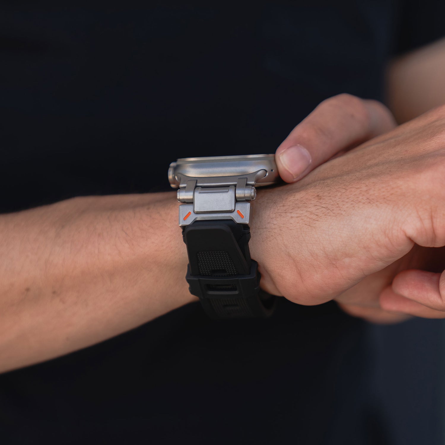 Eine Person im schwarzen Hemd rückt das Arktisband Apple Watch Ultra Armband „Atlas“ an ihrem linken Handgelenk zurecht. Der Fokus liegt auf Uhr und Zeiger, wodurch das robuste Armband mit markanten Edelstahlelementen vor dunklem Hintergrund hervorgehoben wird.