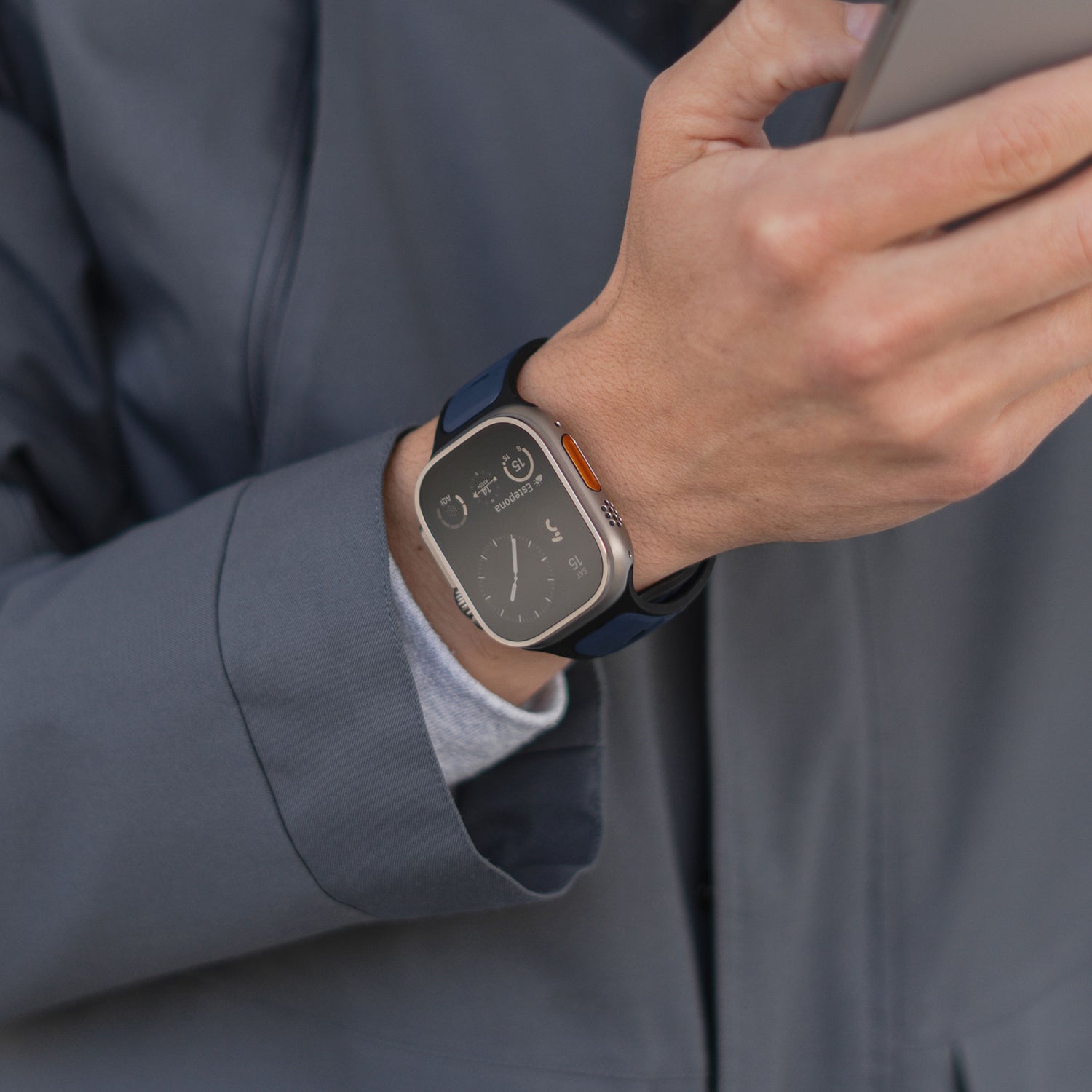 Eine Person in einer grauen Jacke hält ein Smartphone, an ihrem Handgelenk ist ein arktisband Apple Watch Silikonarmband „Swift“ – ein schweißabsorbierendes, atmungsaktives Silikonband – von arktisband zu sehen.