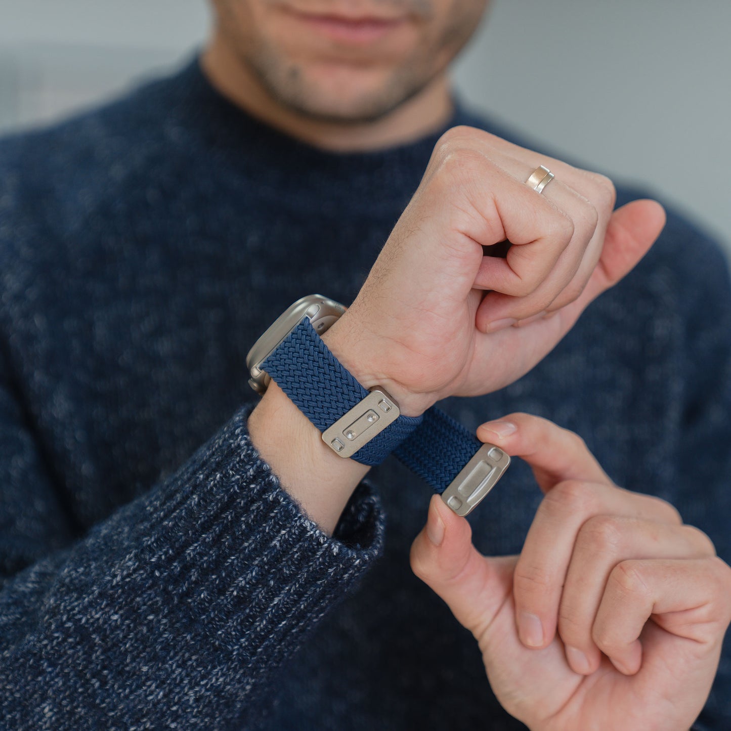 Jemand befestigt das arktisband „Geflochtenes Apple Watch Ultra Armband ‚Casual‘“ mit Magnetverschluss von arktisband am Handgelenk, während er einen dunklen Pullover und einen Ring trägt.