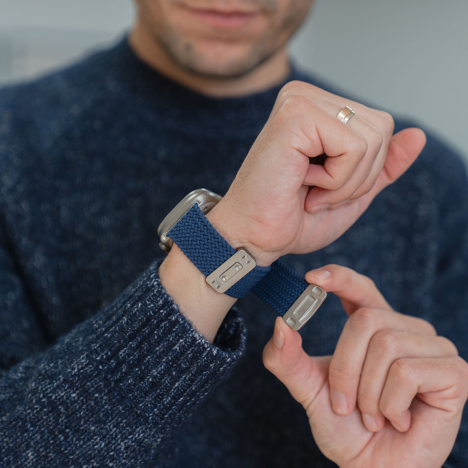 Jemand befestigt das arktisband „Geflochtenes Apple Watch Ultra Armband ‚Casual‘“ mit Magnetverschluss von arktisband am Handgelenk, während er einen dunklen Pullover und einen Ring trägt.