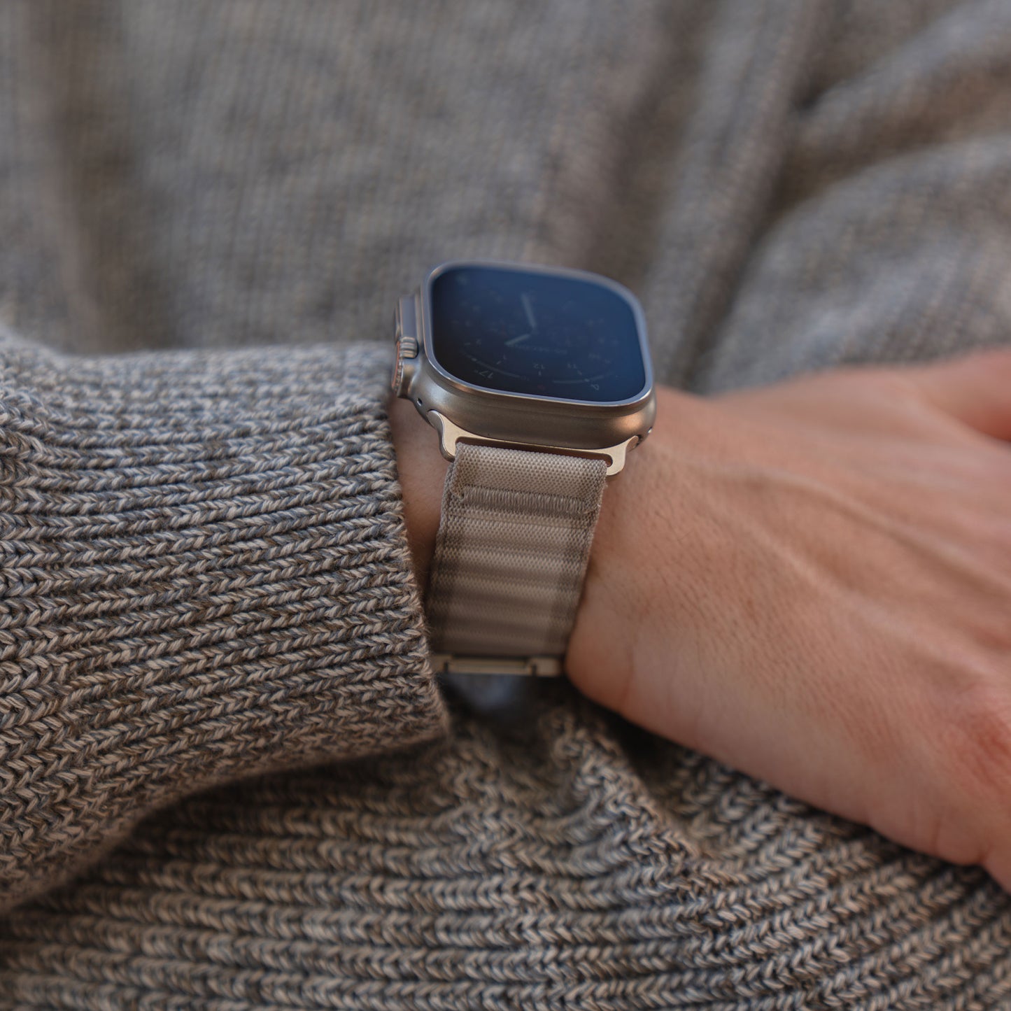 Eine Person trägt das arktisband Apple Watch Armband "CoreX" mit einem Nylonband und Parachute-Verschluss über einem grauen Strickpullover.