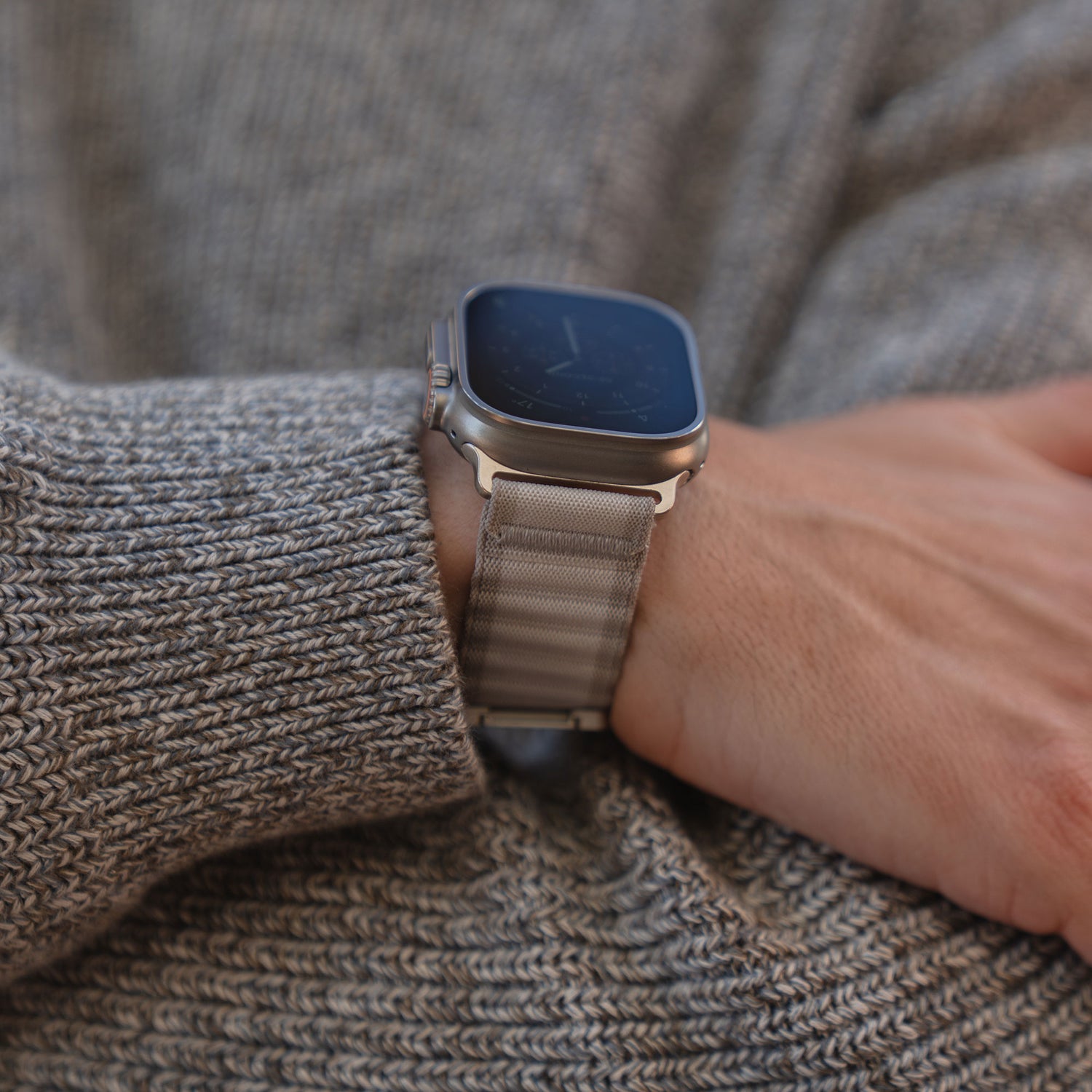 Eine Person trägt das arktisband Apple Watch Armband "CoreX" mit einem Nylonband und Parachute-Verschluss über einem grauen Strickpullover.