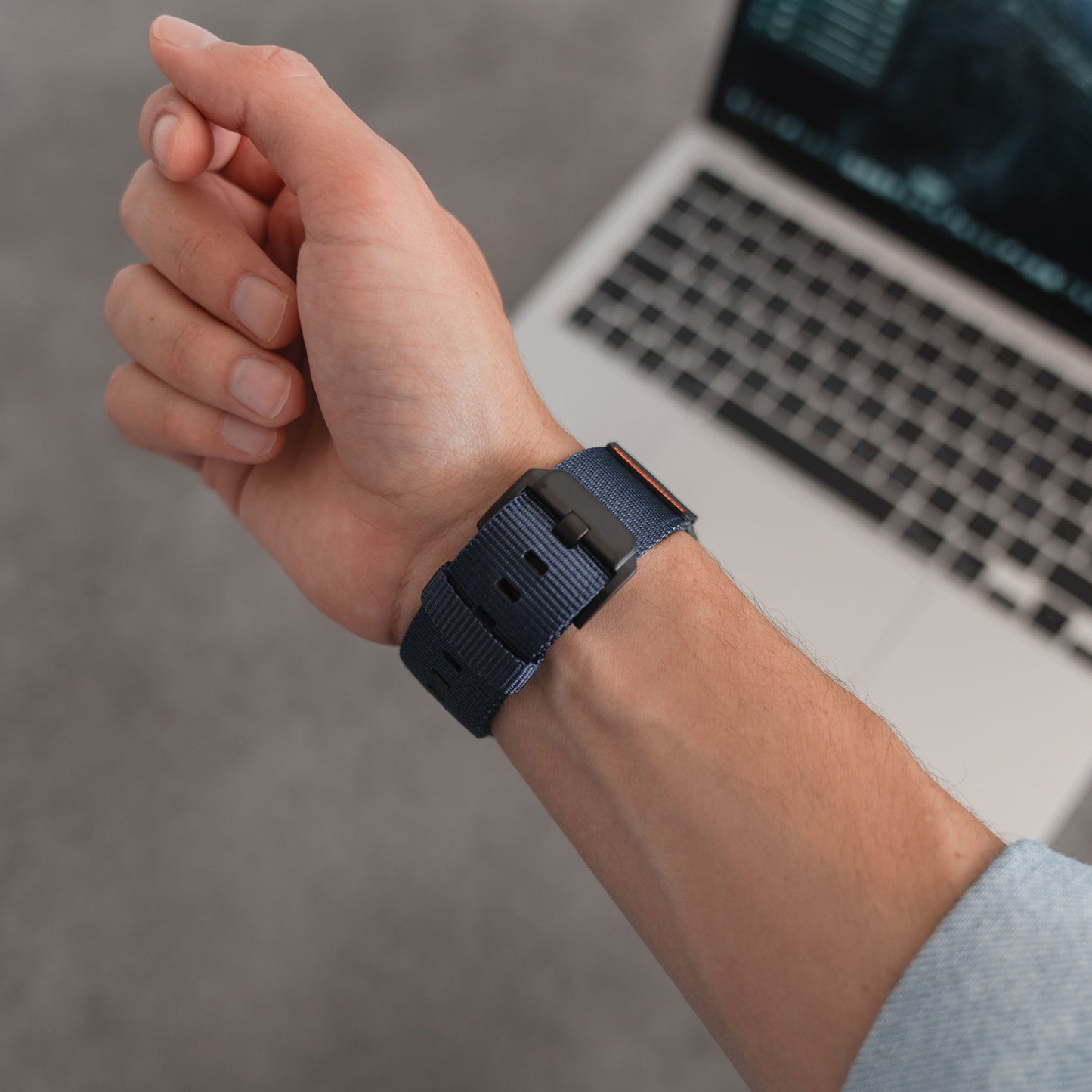 Eine Hand, die ein Arktisband Apple Watch Armband "Terra" in Marineblau (extrabreit, 24 mm Nylon) trägt, wird über eine Laptop-Tastatur auf einer grauen Oberfläche gehalten.