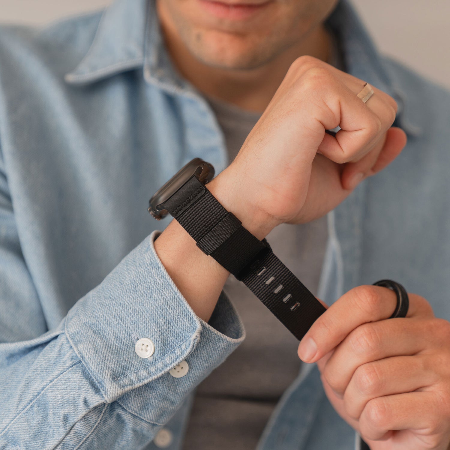 Eine Person, die das arktisband Apple Watch Armband "Terra" von arktisband trägt, sichert ihre Apple Watch Ultra an ihrem Handgelenk, bekleidet mit einem hellen Jeanshemd.