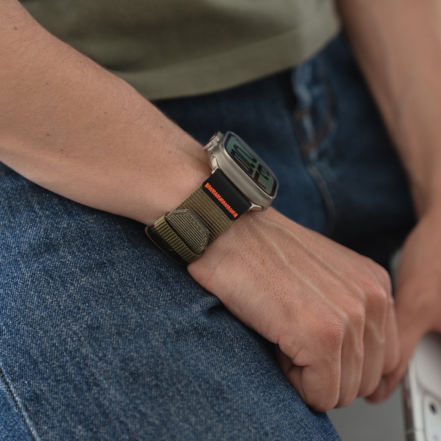 Eine Person trägt das arktisband Apple Watch Armband "Terra" von arktisband mit einem extrabreiten 24 mm Nylonband und sitzt in einer blauen Jeans.