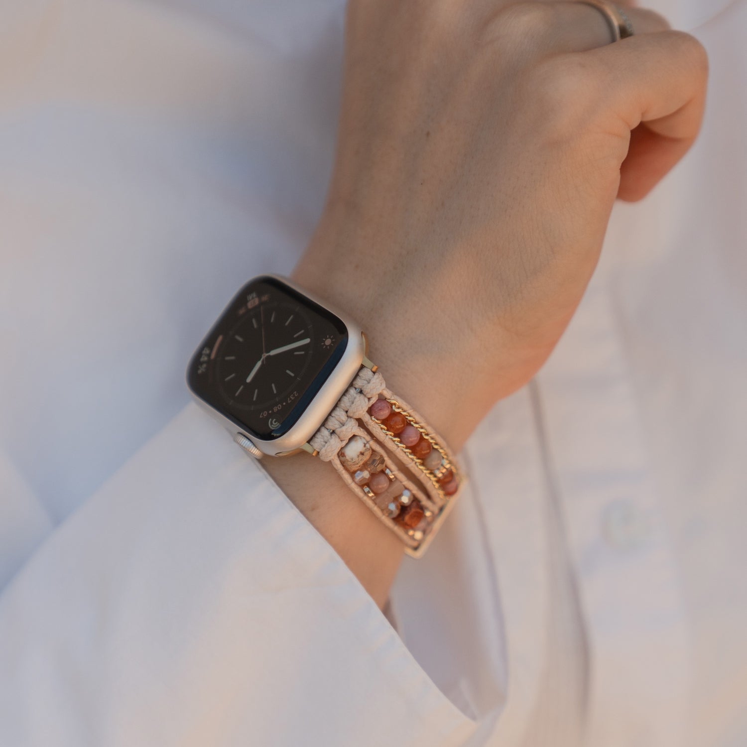 Eine Person, die das Arktisband Apple Watch-Armband „Sunset Spirit“ mit Zierperlen und ein weißes Langarmhemd trägt.