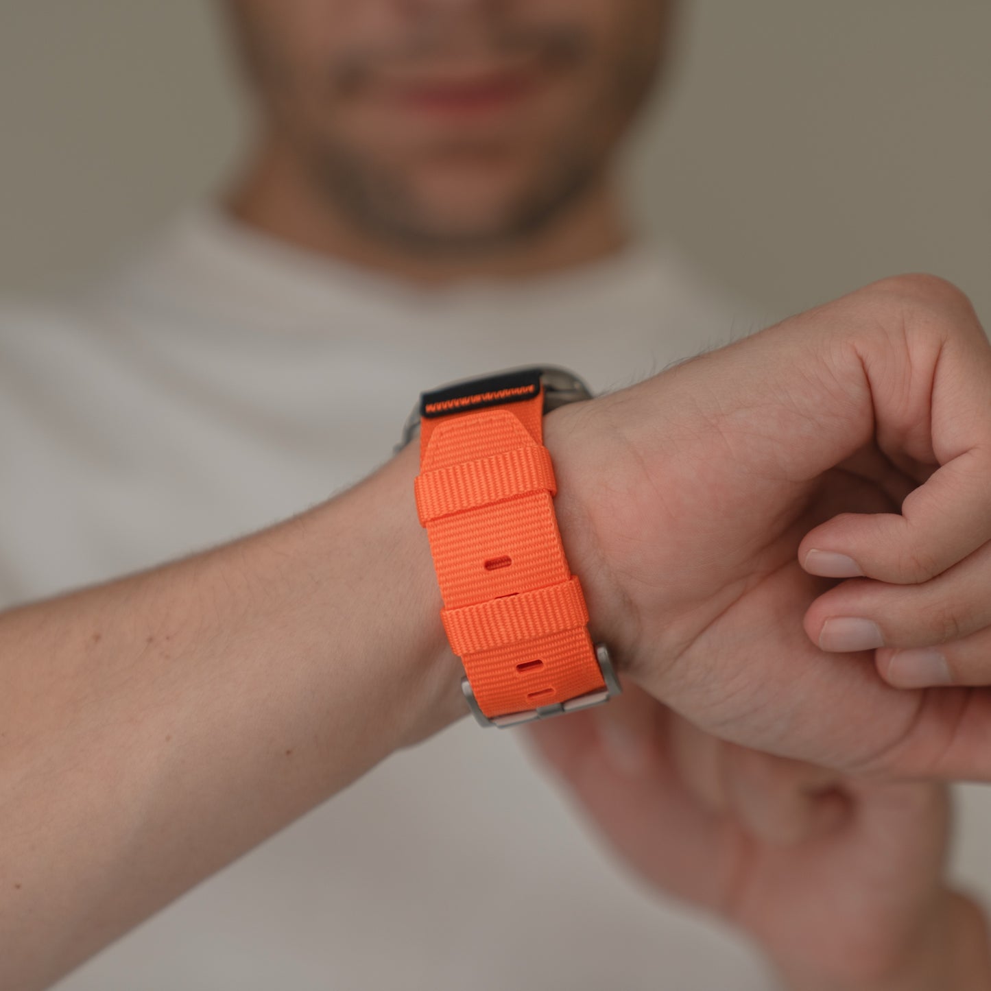 Eine Person passt das arktisband Apple Watch Armband "Terra" - ein extra breites, leuchtend orangefarbenes 24-mm-Nylonarmband von arktisband - an ihr Handgelenk an, während sie ein weißes Hemd trägt, ideal für die Apple Watch Ultra.