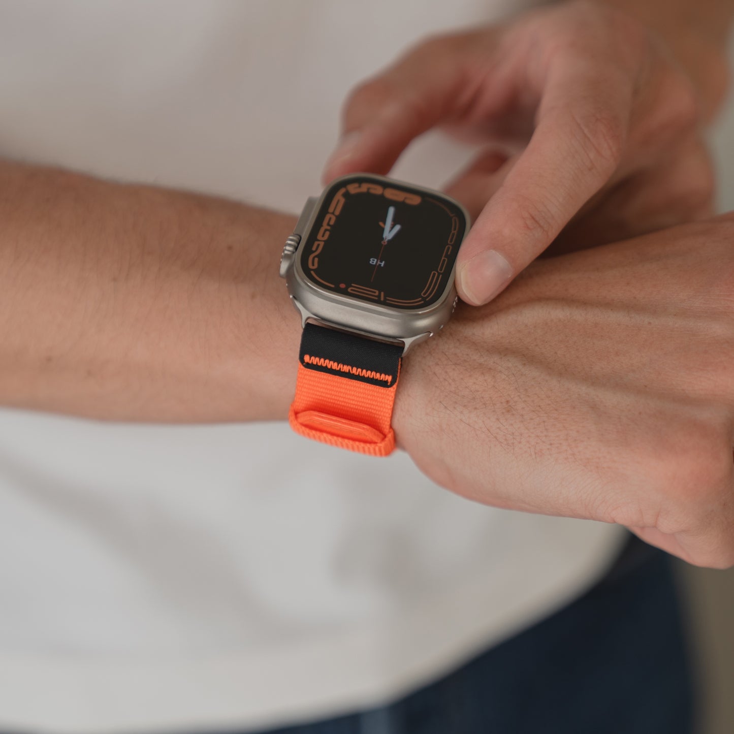 Eine Person trägt ein arktisband Apple Watch Armband "Terra" mit einem extrabreites 24 mm Nylonband in Orange an ihrer Apple Watch Ultra und tippt mit dem Finger auf den Bildschirm.