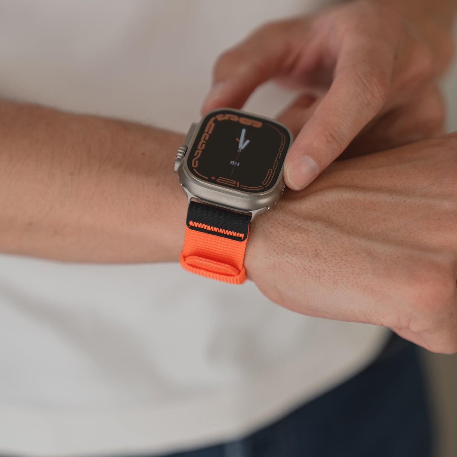 Eine Person trägt ein arktisband Apple Watch Armband "Terra" mit einem extrabreites 24 mm Nylonband in Orange an ihrer Apple Watch Ultra und tippt mit dem Finger auf den Bildschirm.