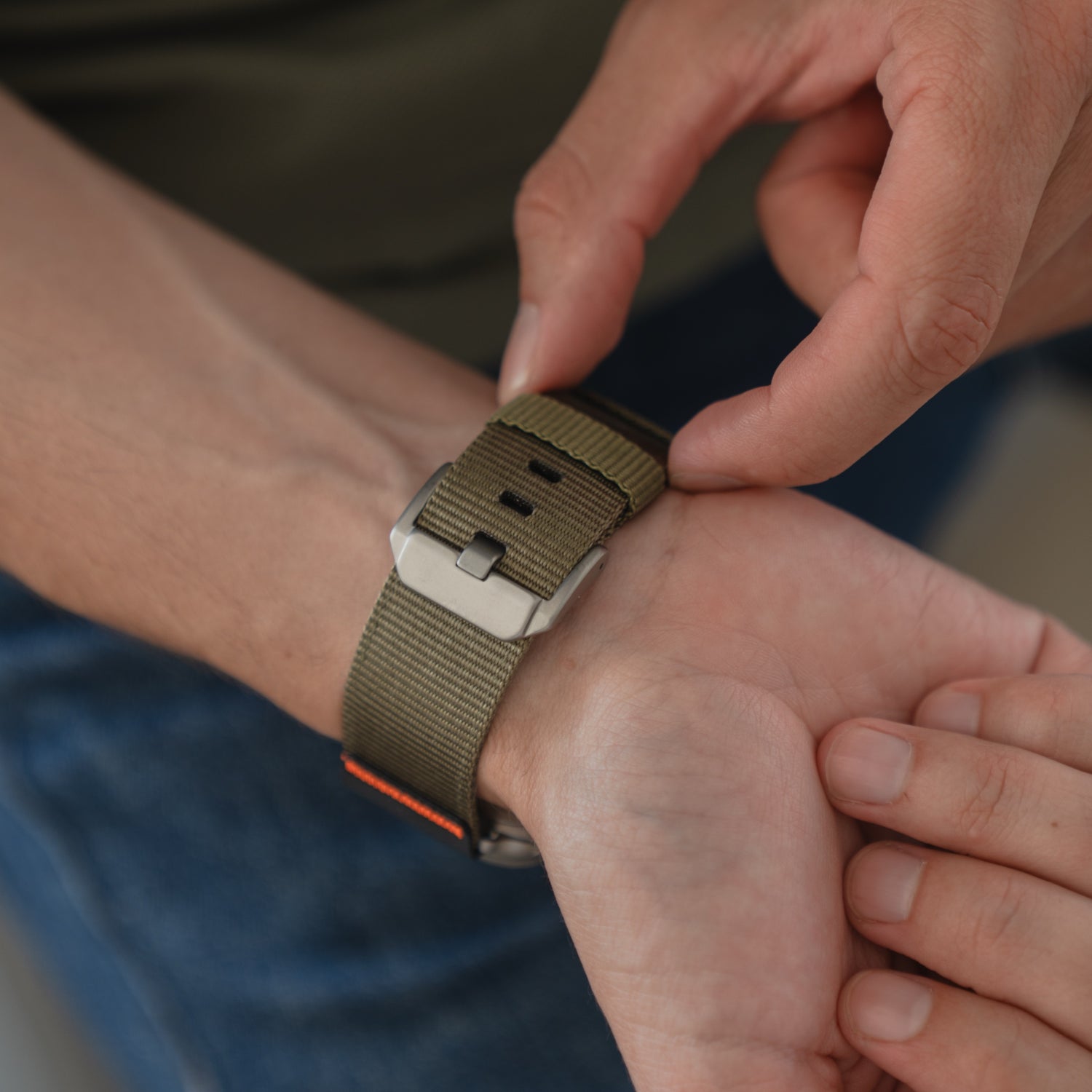 Nahaufnahme der Hände, die ein arktisband Apple Watch Armband "Terra" mit einem 24-mm-Nylonband und einer silbernen Schnalle an einem Handgelenk befestigen.