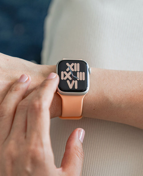 Eine Frau trägt ein pfirsichfarbenes Apple Watch Silikonarmband.