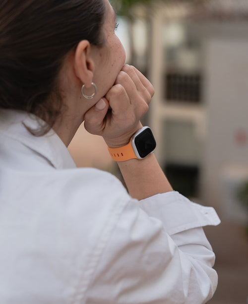 Orangenes Apple Watch Silikonarmband an einem Handgelenk.