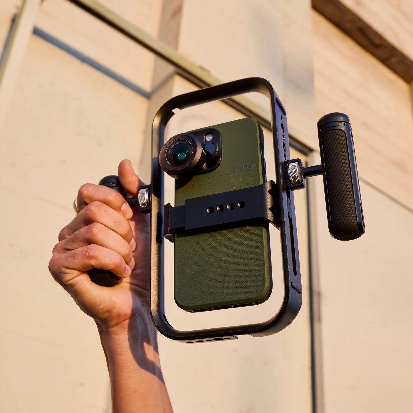Eine Hand hält den MOMENT Basecage - einen schnellen und leichten mobilen Käfig für Smartphones, der mit einer Objektivbefestigung und zwei Griffen ausgestattet ist und damit das perfekte iPhone-Rig für Filmemacher darstellt.
