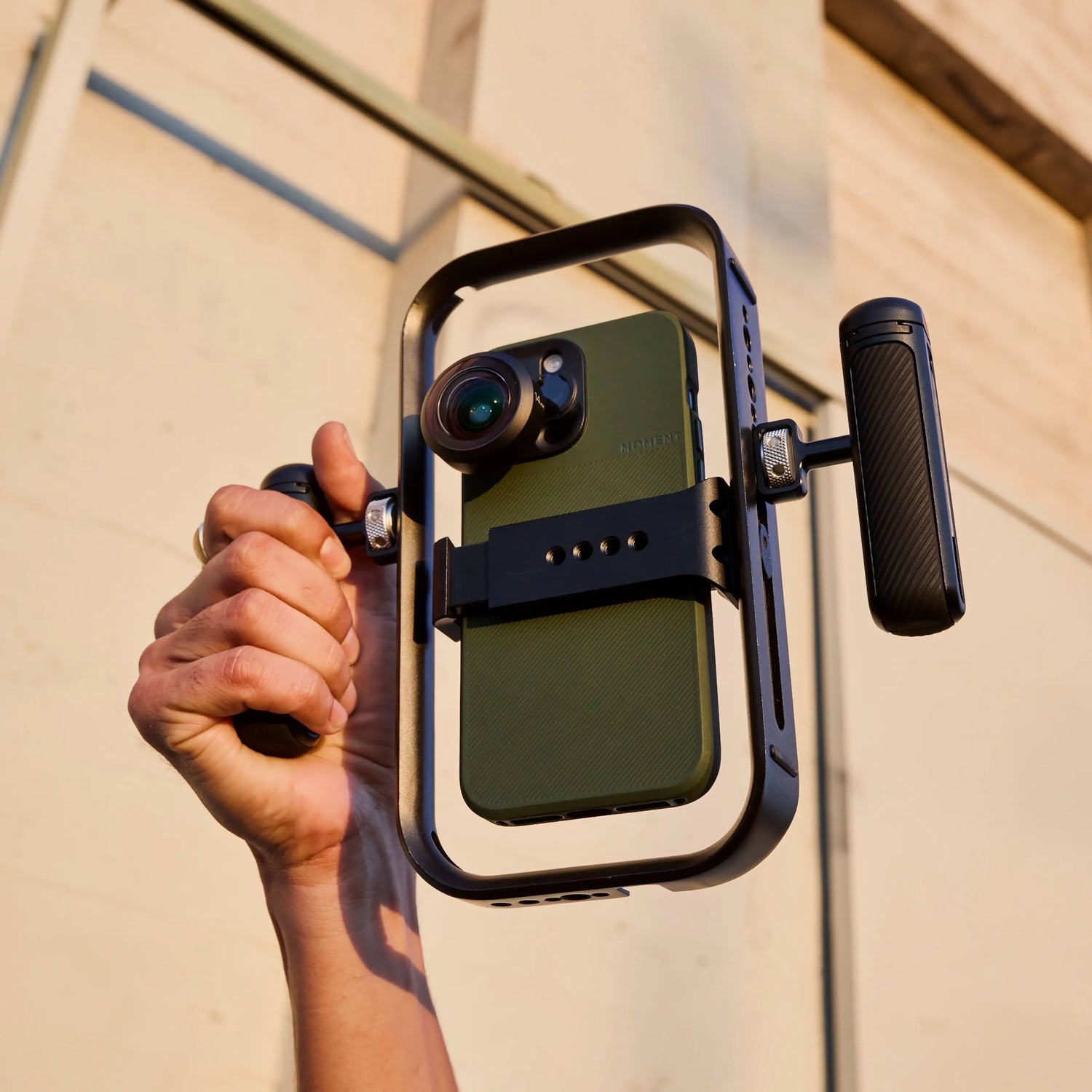 Eine Hand hält den MOMENT Basecage - einen schnellen und leichten mobilen Käfig für Smartphones, der mit einer Objektivbefestigung und zwei Griffen ausgestattet ist und damit das perfekte iPhone-Rig für Filmemacher darstellt.