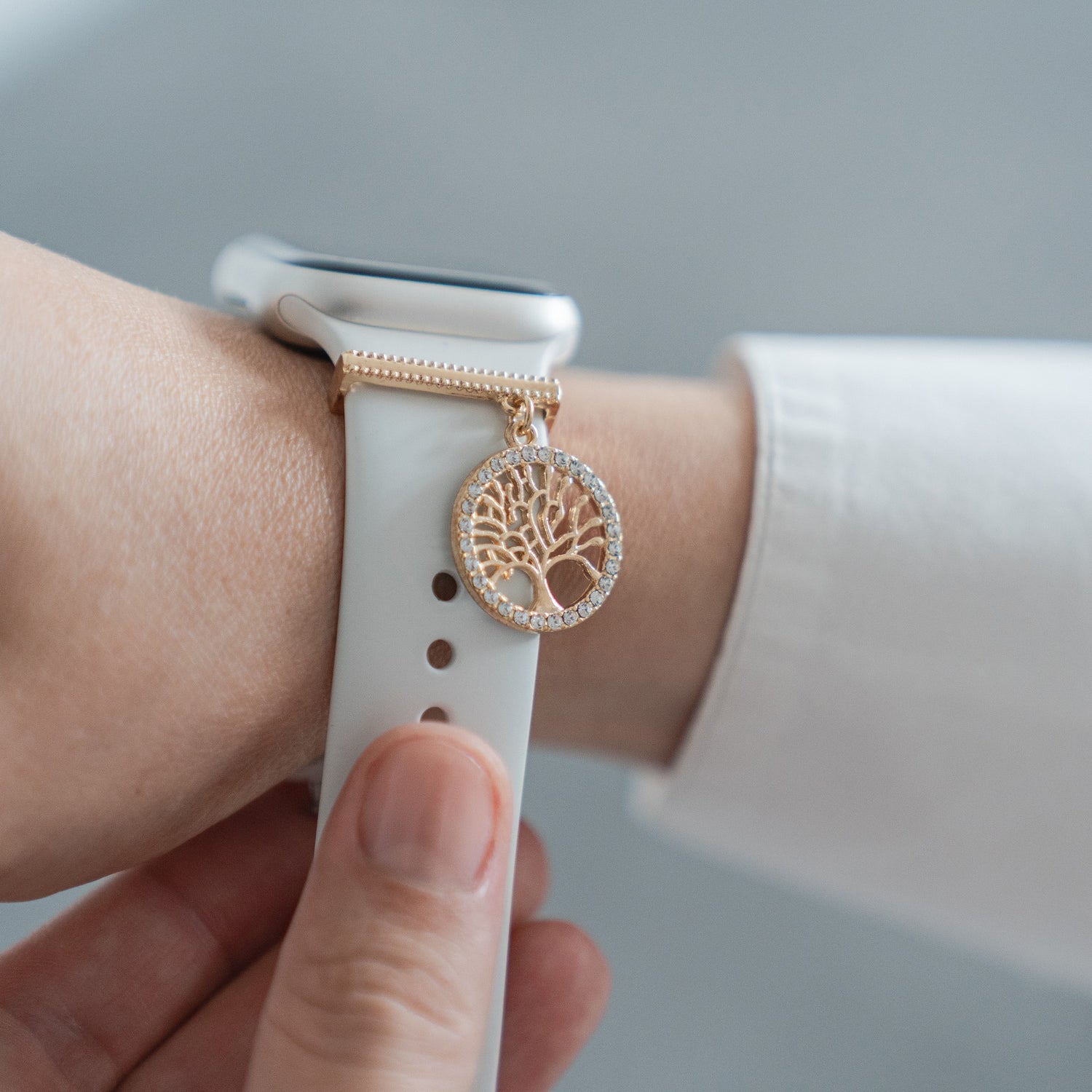 Eine Hand trägt einen arktisband Apple Watch Charms „Baum des Lebens“ – Gold, ein stylisches Accessoire von arktisband, das jedem Outfit einen goldenen Akzent verleiht.