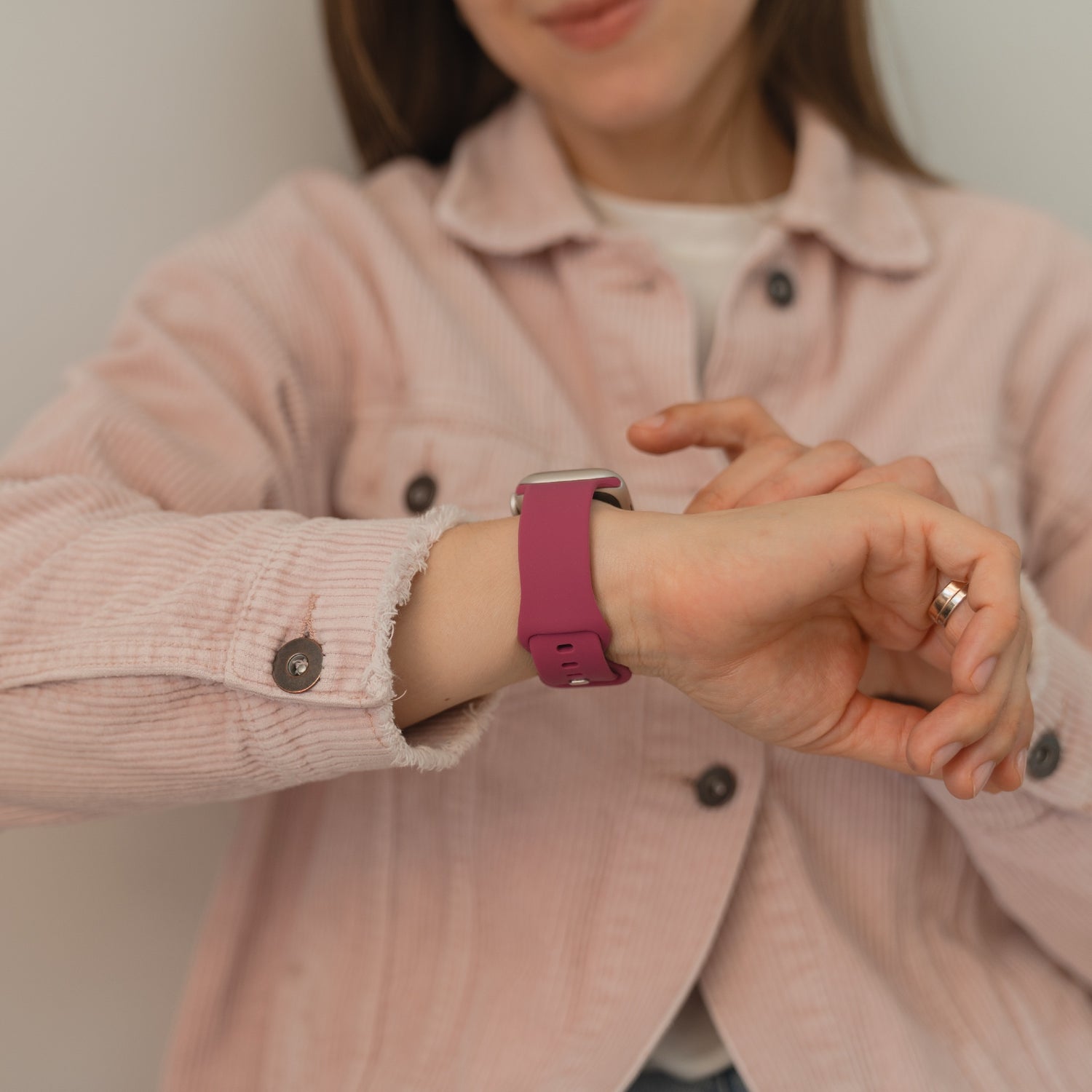 Eine Frau in rosa Jacke kontrolliert ihre Smartwatch und trägt am linken Handgelenk das arktisband Apple Watch Silikonarmband "Sport" in Lila von arktisband - mit seinem sportlichen, schweißabsorbierenden Design perfekt für aktive Tage.