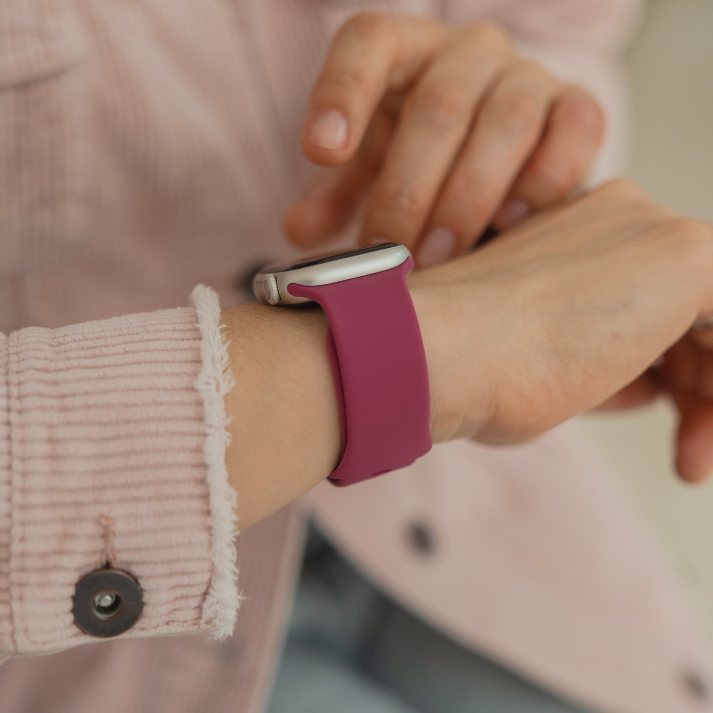 Eine Person, die ein rosa arktisband Apple Watch Silikonarmband "Sport" von arktisband trägt, berührt den Bildschirm, während sie eine rosa Jacke trägt.