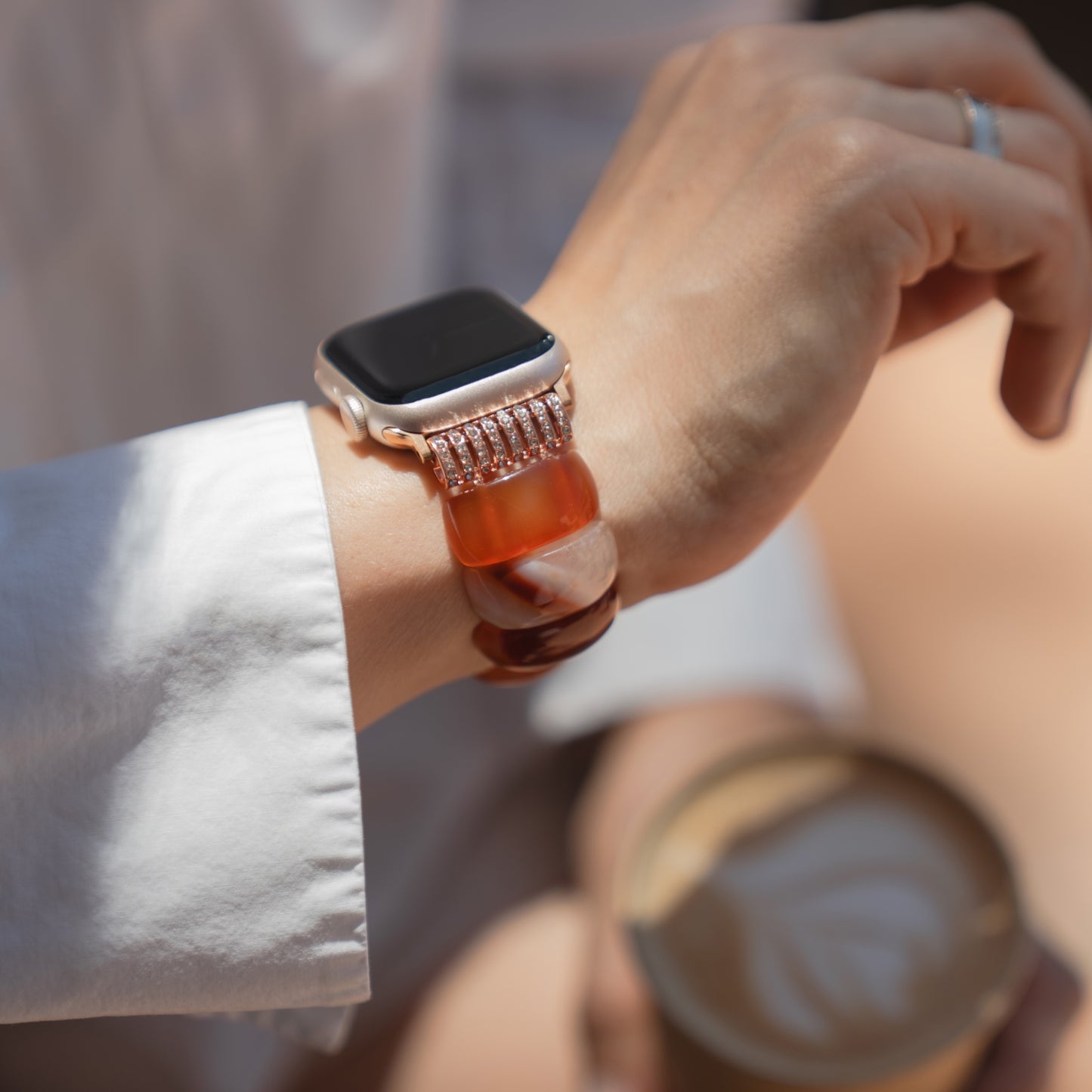 Eine Person, die das arktisband Apple Watch-Armband „Stone Pearl“ von arktisband trägt, hält eine Tasse Kaffee mit Latte-Art in der Hand.