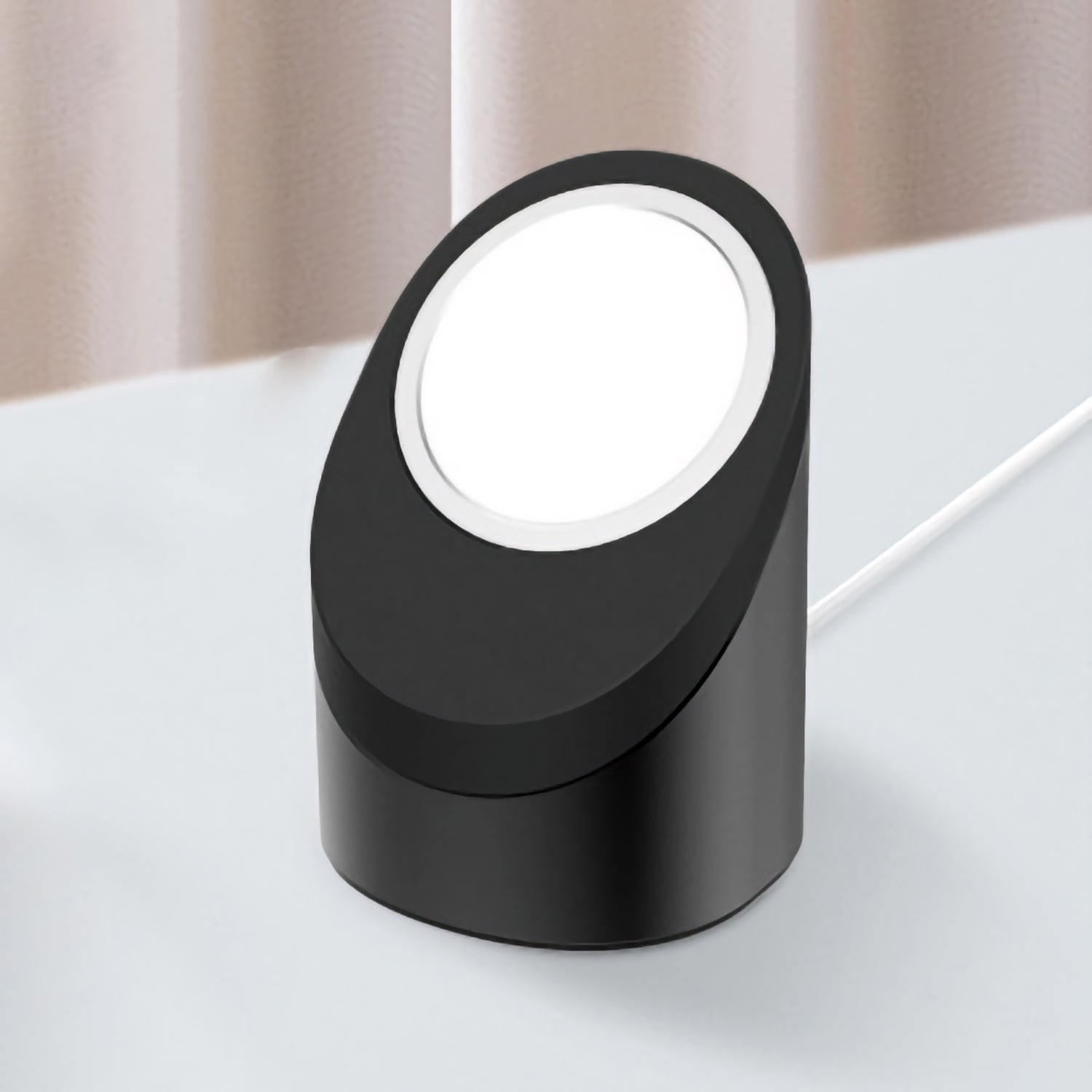 Eine kompakte, schwarze, ovale LED-Schreibtischlampe mit weißem Licht steht neben dem arktis MagSafe NightStand, einem eleganten Organizer von arktis für Ihre iPhone Ladestation, auf einer weißen Fläche.