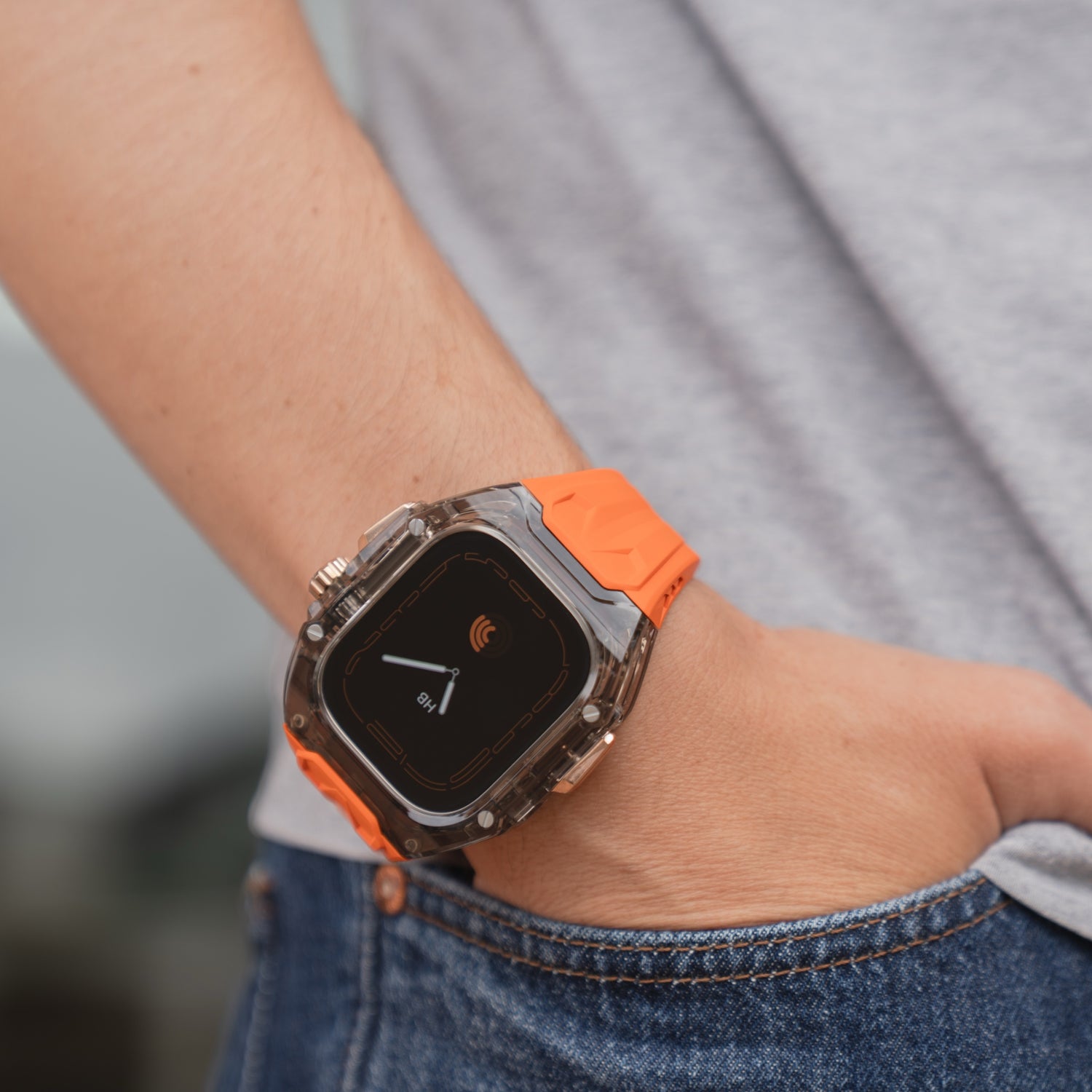 Eine Person trägt das arktisband Apple Watch Armband "Armor Fusion" mit orangefarbenem Silikonarmband und transparentem, stoßfestem Gehäuse, das ein Symbol für kontaktloses Bezahlen zeigt.