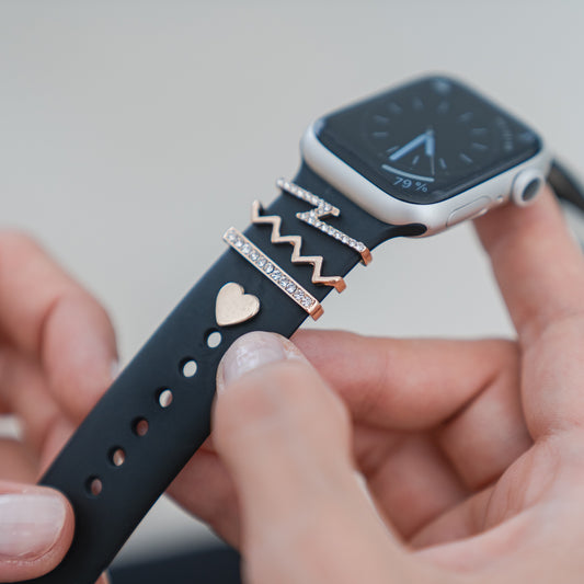 Eine Hand befestigt Arktisband-Apple-Watch-Charms „Golden Lightning“ – Gold an einem schwarzen Band und verleiht Ihrem Arktisband oder jedem Apple-Watch-Armband Glanz und Stil.