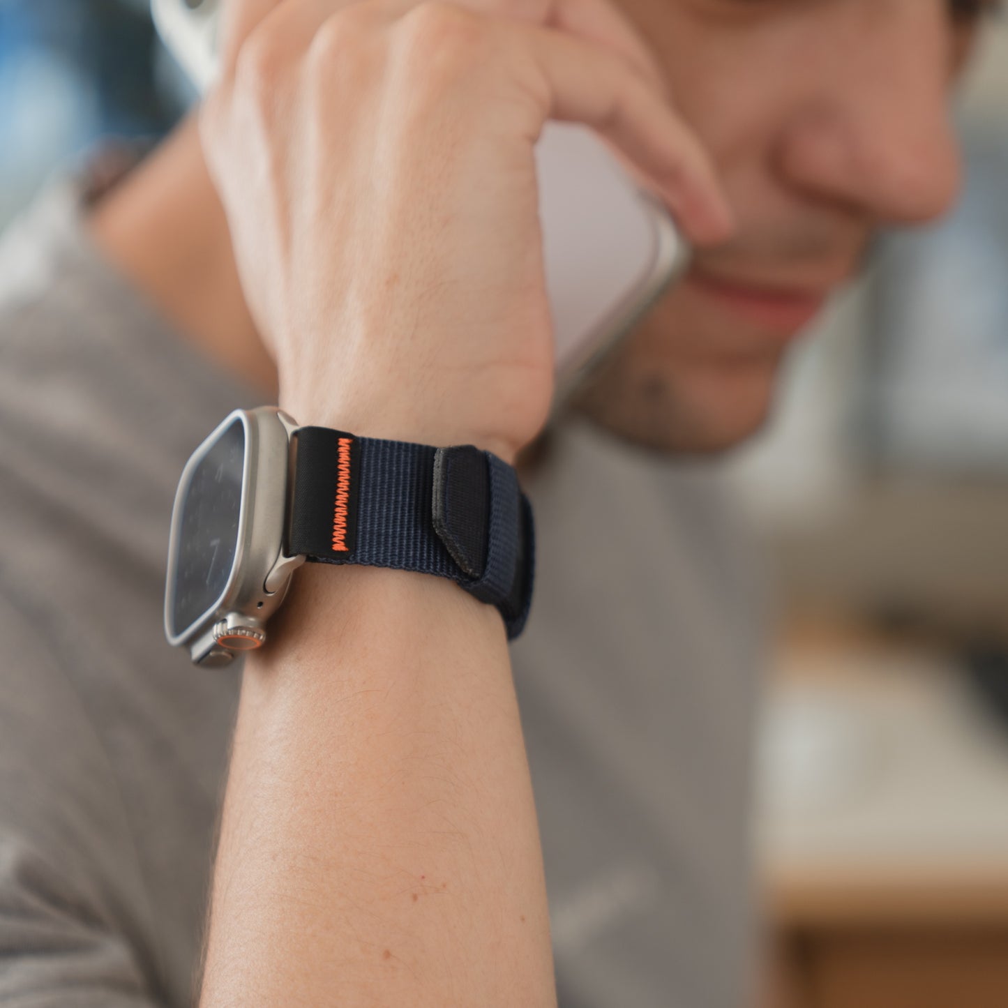 Eine Person trägt ein arktisband Apple Watch Armband "Terra" von arktisband mit einem 24 mm breiten Nylonband und hält ein Telefon an ihr Ohr.
