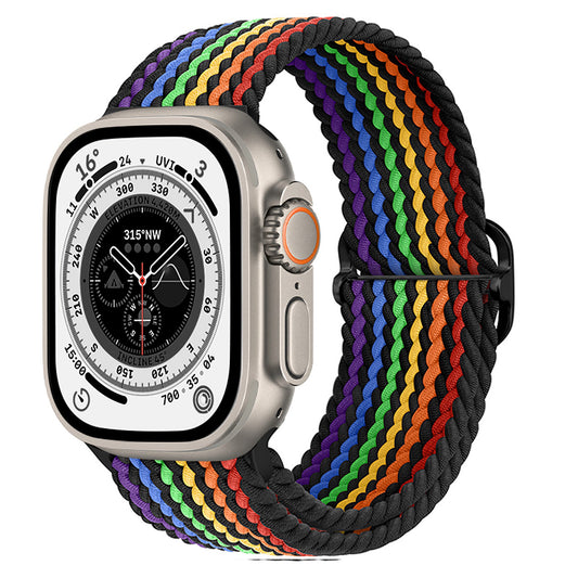 Eine Smartwatch mit silbernem Gehäuse und runder digitaler Kompassanzeige, abgebildet mit dem geflochtenen Flex Loop Pride Armband von arktisband für die Apple Watch – einem gewebten Nylonband mit Regenbogenmuster und schwarzen Rändern von arktisband.