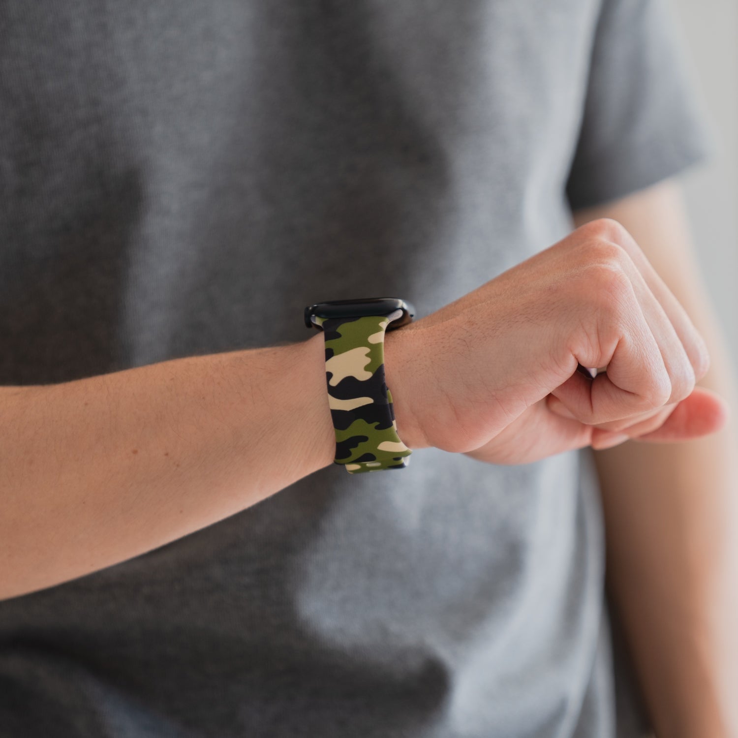 Ein Träger eines grauen T-Shirts trägt das arktisband Camouflage Apple Watch Armband, ein stylisches Accessoire von arktisband, das jeder Apple Watch einen einzigartigen Touch verleiht.