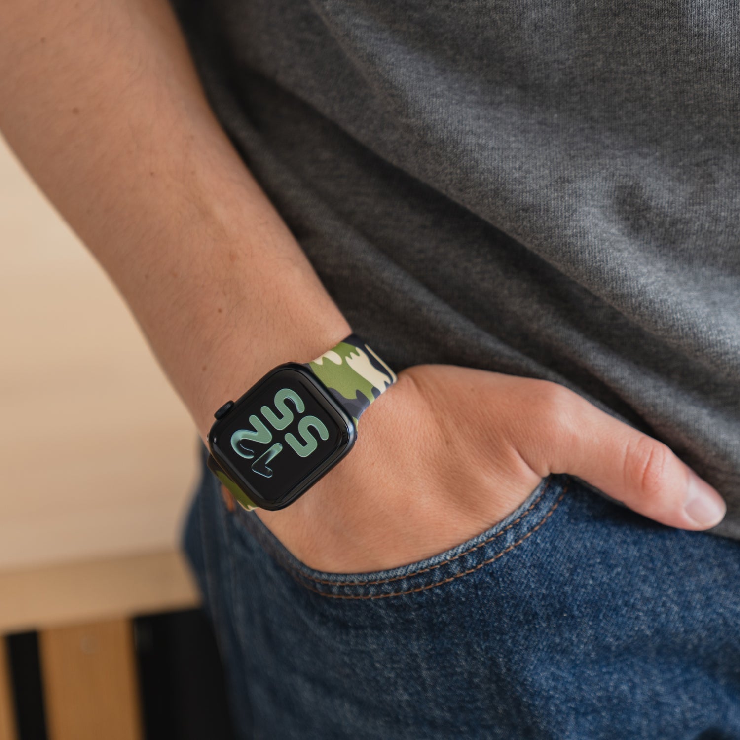 Die Person trägt ein arktisband Camouflage Apple Watch Armband von arktisband, die Hand in der Jeanstasche und ein graues T-Shirt für einen lässigen, sportlichen Stil.