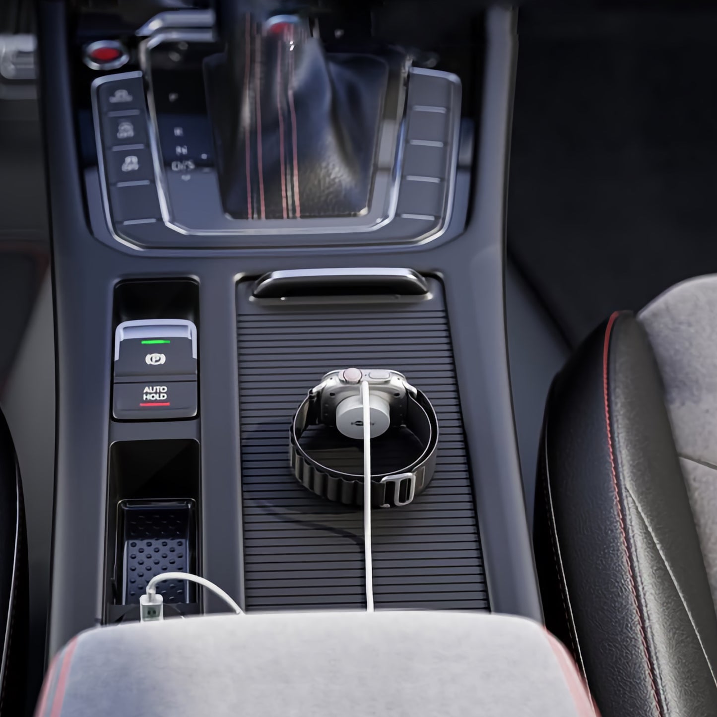 Ein Goobay Magnetisches Ladegerät für Apple Watch 1 m lädt eine Smartwatch kabellos auf der Mittelkonsole eines Autos auf, neben dem Schalthebel und umgeben von Knöpfen und rot genähten Sitzen.