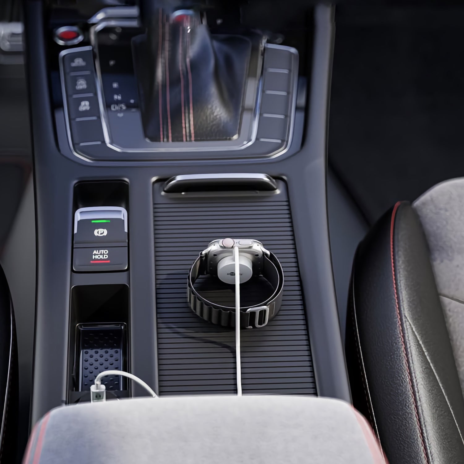 Ein Goobay Magnetisches Ladegerät für Apple Watch 1 m lädt eine Smartwatch kabellos auf der Mittelkonsole eines Autos auf, neben dem Schalthebel und umgeben von Knöpfen und rot genähten Sitzen.