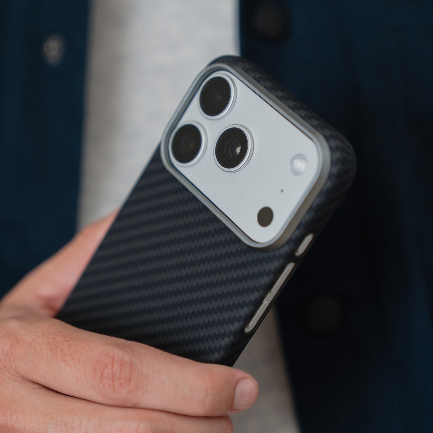 Eine Hand hält ein arktis iPhone 17 Pro Carbon Case - kompatibel mit MagSafe, schwarzes Carbon-Finish - auf einem Smartphone mit dreifacher Rückkamera.