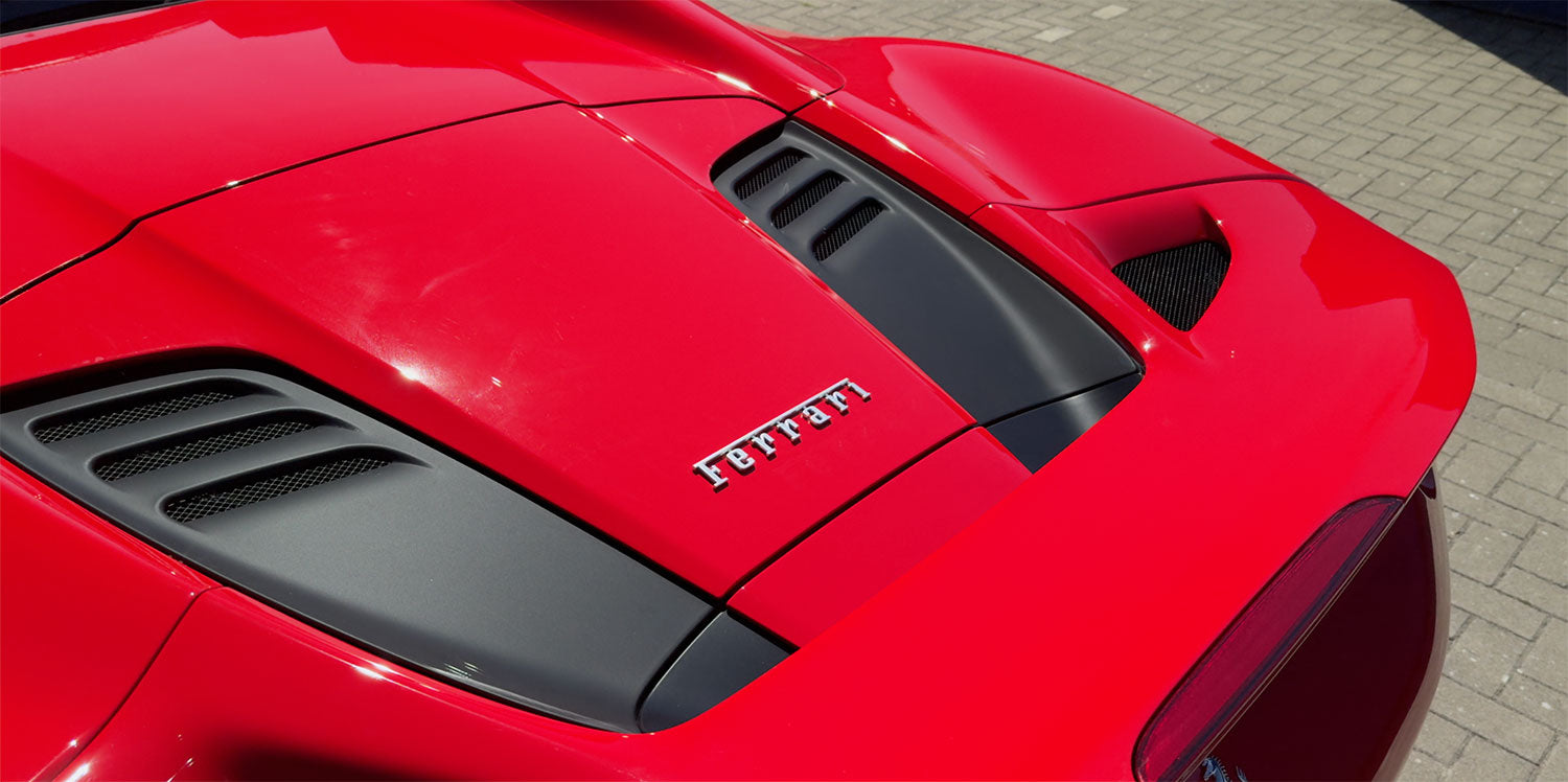 Nahaufnahme der hinteren Motorabdeckung eines roten Ferrari-Sportwagens mit schwarzen Lüftungsschlitzen und dem Ferrari-Logo.