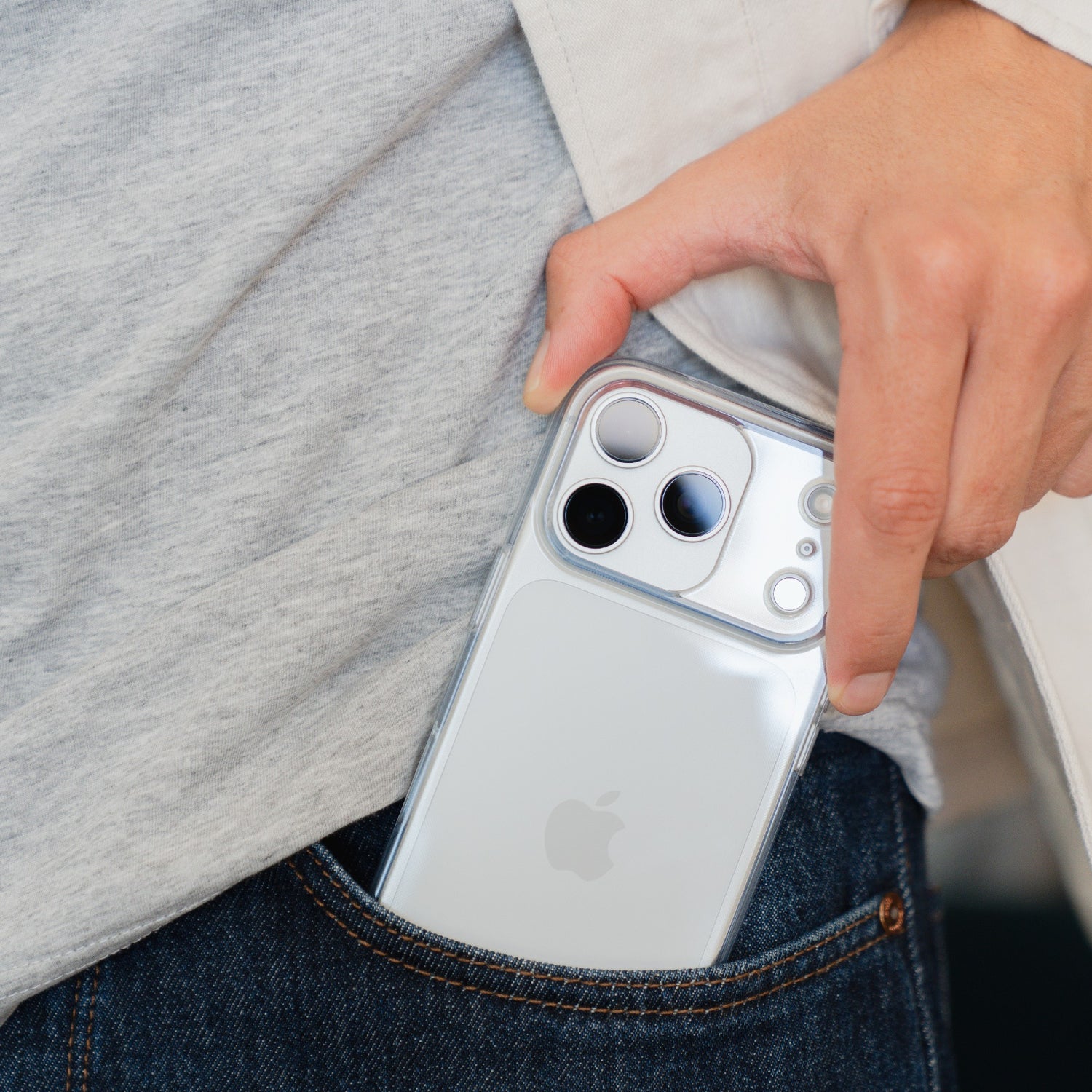 Eine Hand schiebt ein silbernes iPhone mit dem arktis iPhone 17 Pro Max Invisible Case, einer transparenten und stoßfesten Hülle von arktis, in die Vordertasche einer Blue Jeans.