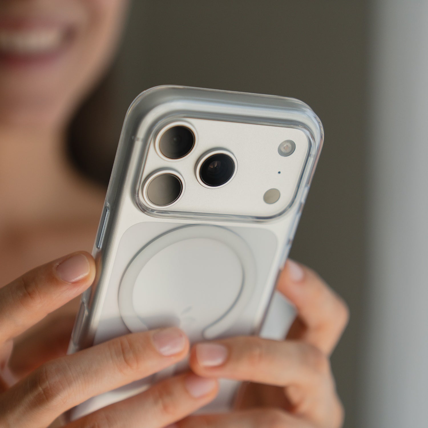 Eine Person hält ein arktis iPhone 17 Pro Max PureCase mit MagSafe Transparent Case auf einem weißen iPhone und lächelt im Hintergrund.
