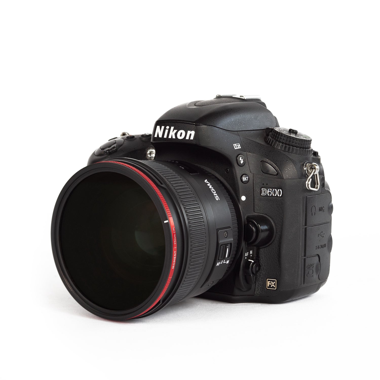 Eine schwarze Nikon D600 DSLR-Kamera mit einem großen Sigma-Objektiv und Kamera-Zubehör wie dem Moment 67mm AntiGlare CPL Filter von MOMENT vor einem weißen Hintergrund.