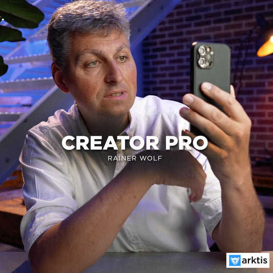 Ein Mann mit grauen Haaren und weißem Hemd blickt auf sein Smartphone. Auf dem Display erscheint der Text „Creator Pro by Rainer Wolf“, rechts unten das Arktis-Logo.