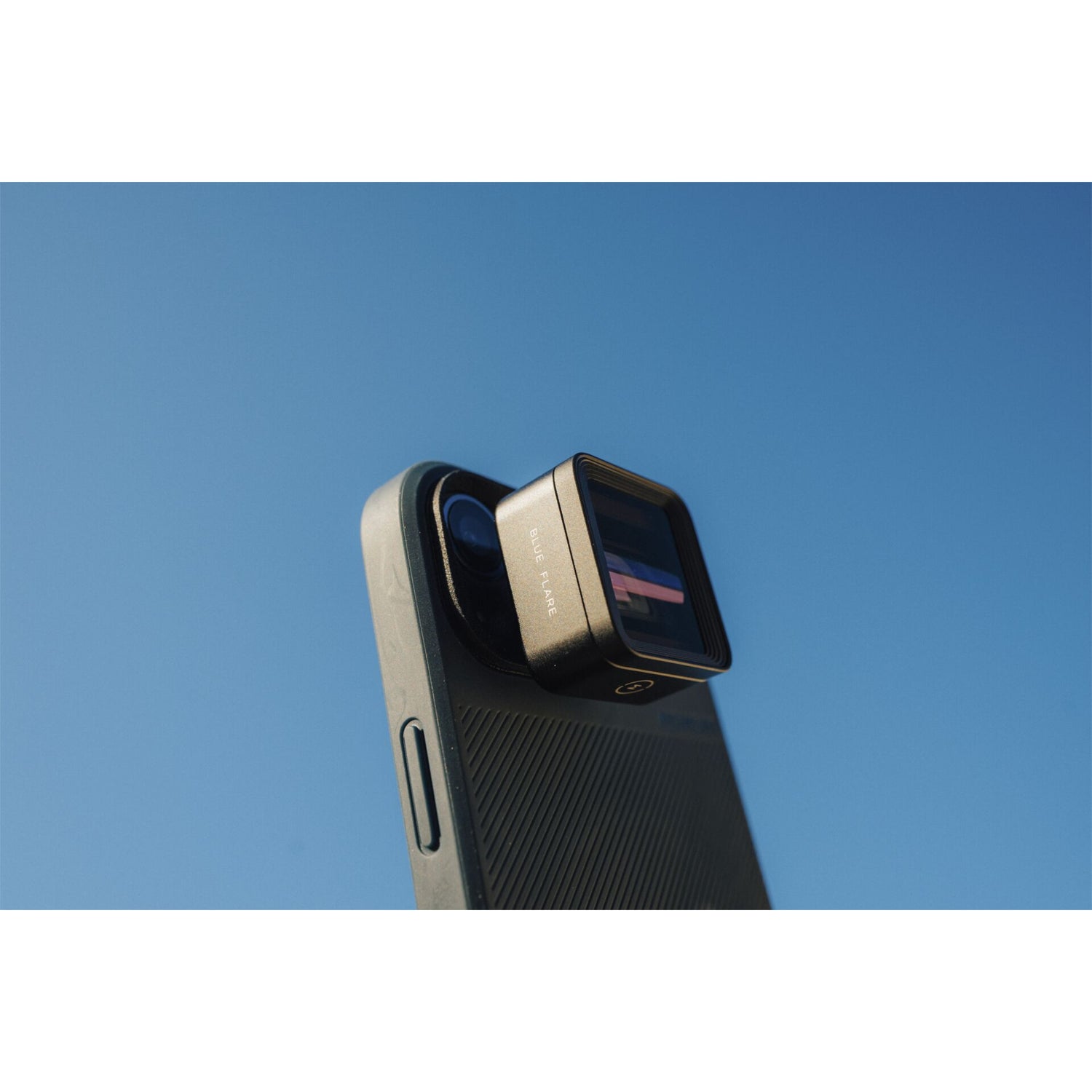 Nahaufnahme eines Smartphones mit aufgesetztem MOMENT 1,33x Anamorphot-Objektiv der T-Serie vor einem klaren blauen Himmel - ideal für filmische Smartphone-Aufnahmen.