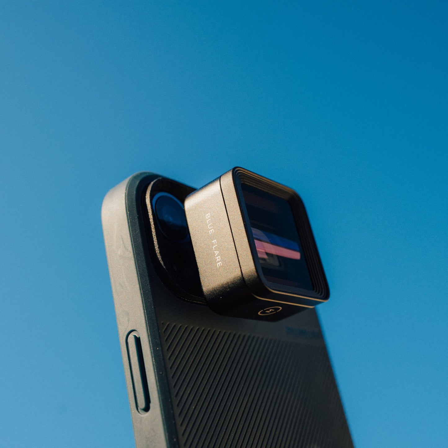 Nahaufnahme einer Smartphone-Kamera mit angesetztem MOMENT 1,55x Anamorphot-Objektiv der T-Serie vor einem klaren blauen Himmel.