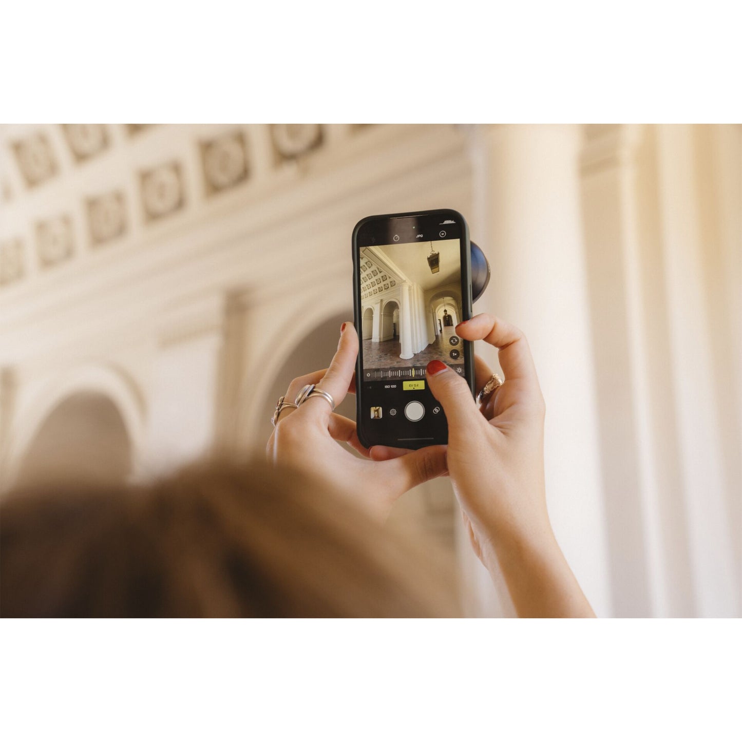 Jemand fotografiert kunstvolle Innenarchitektur von hinten mit einem Smartphone und verwendet das MOMENT 18-mm-Weitwinkelobjektiv - T-Serie für eine beeindruckende Weitwinkelaufnahme.