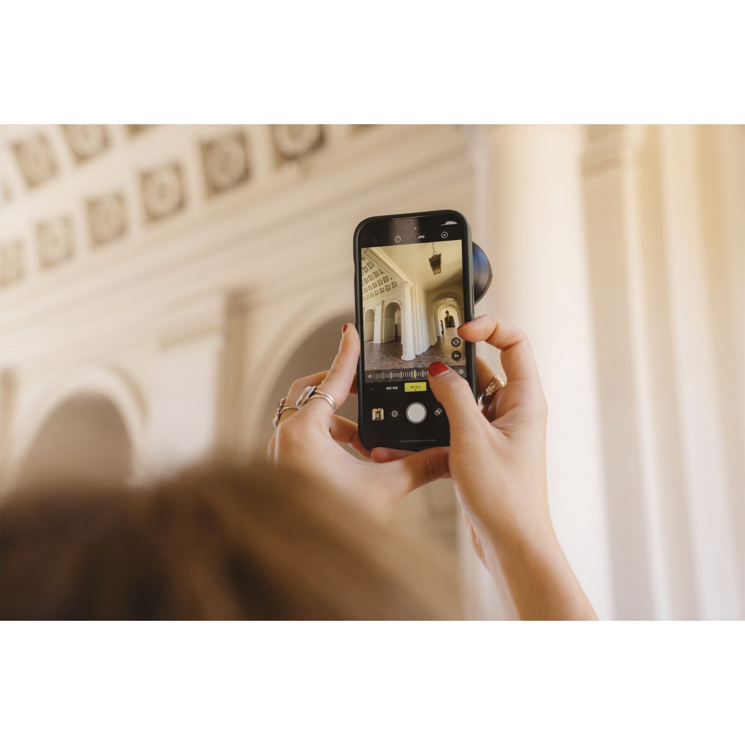 Jemand fotografiert kunstvolle Innenarchitektur von hinten mit einem Smartphone und verwendet das MOMENT 18-mm-Weitwinkelobjektiv - T-Serie für eine beeindruckende Weitwinkelaufnahme.