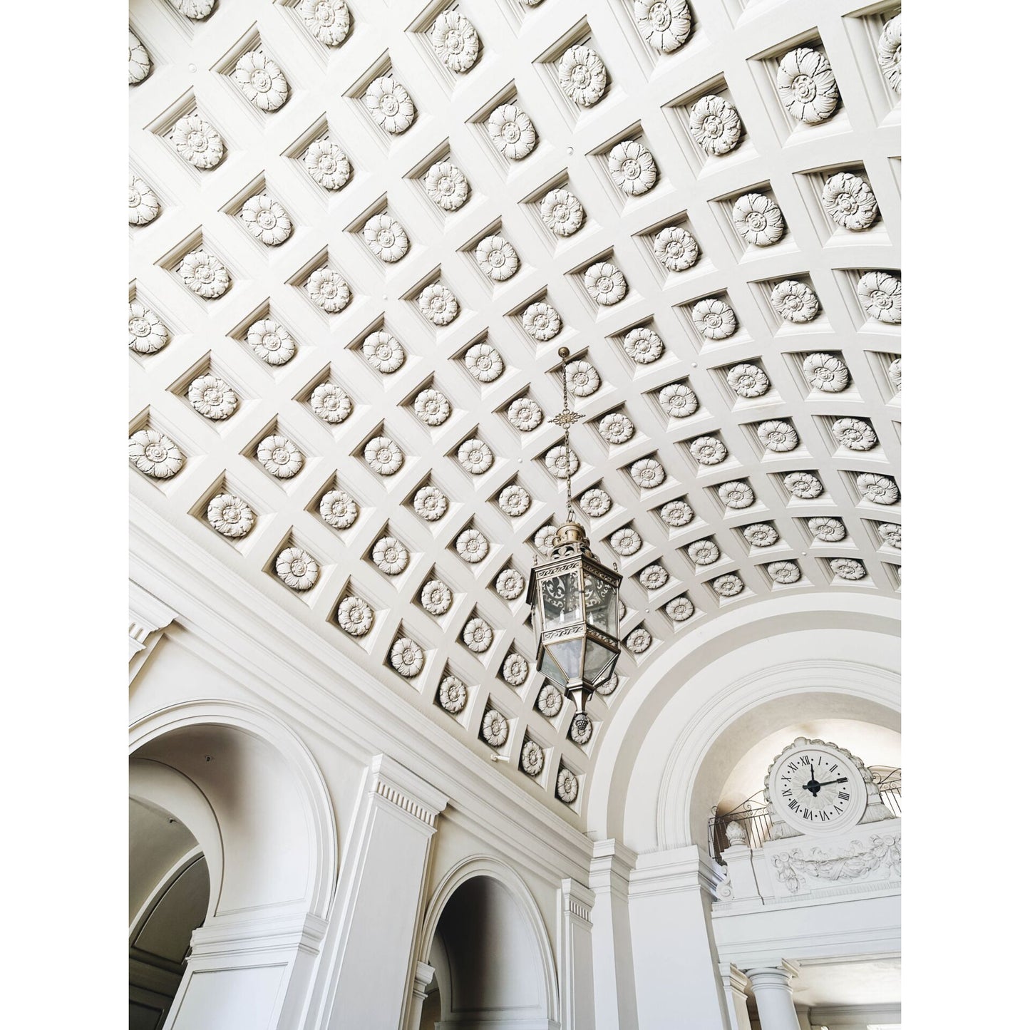 Dekorative weiße Gewölbedecke mit einer hängenden Laterne und einer großen Uhr über gewölbten Türöffnungen, wunderschön eingefangen mit dem MOMENT 18mm Weitwinkelobjektiv - T-Serie für Ihr iPhone-Kamerazubehör.