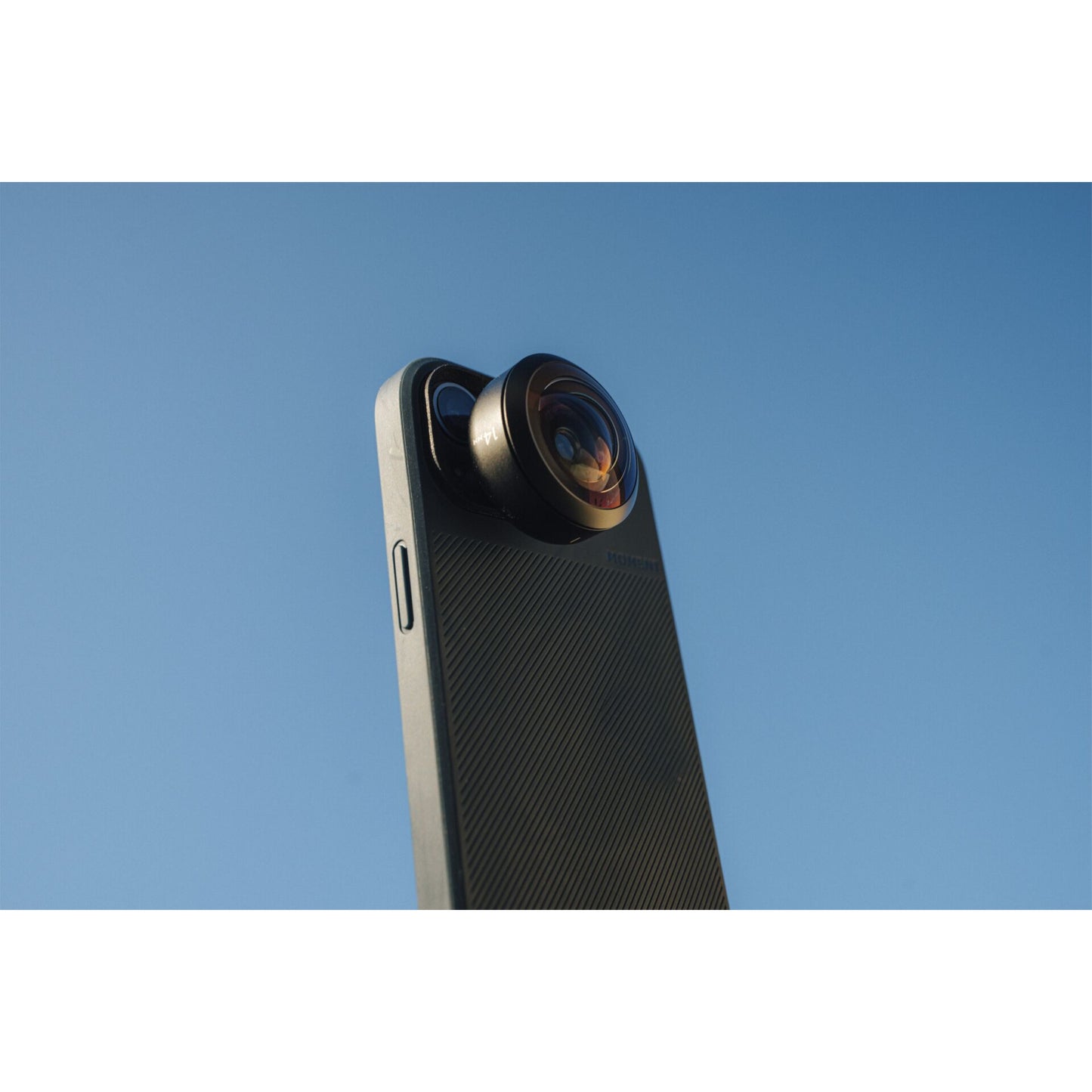 Ein Smartphone mit aufgesetztem MOMENT 14mm Fisheye-Objektiv - T-Serie, gehalten gegen einen klaren blauen Himmel, unterstreicht das hochwertige iPhone Kamera Zubehör für atemberaubende Ultraweitwinkelaufnahmen.