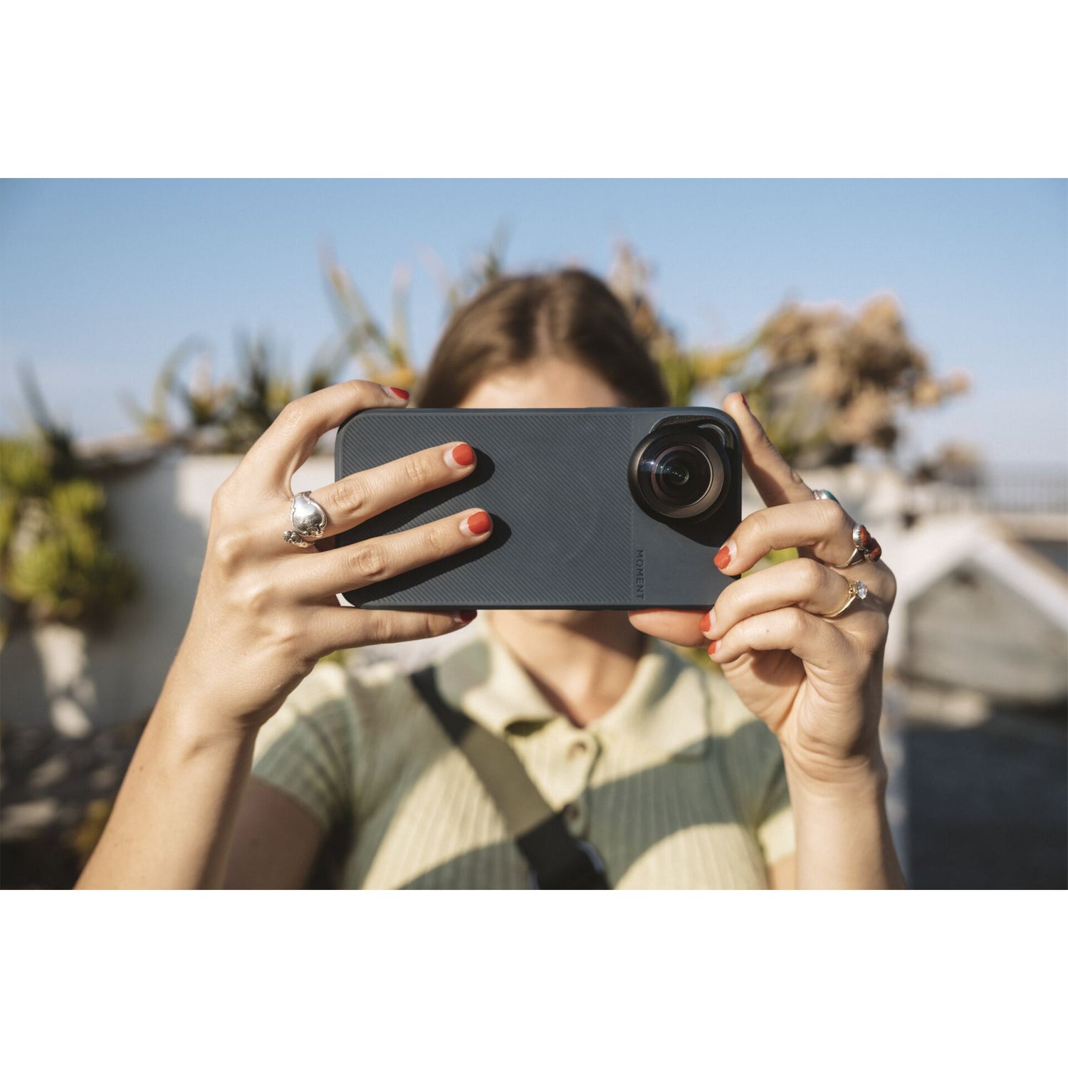 Eine Frau verwendet ein MOMENT 14mm Fisheye-Objektiv der T-Serie an ihrem Smartphone, um an einem sonnigen Tag ein Foto im Freien zu machen.